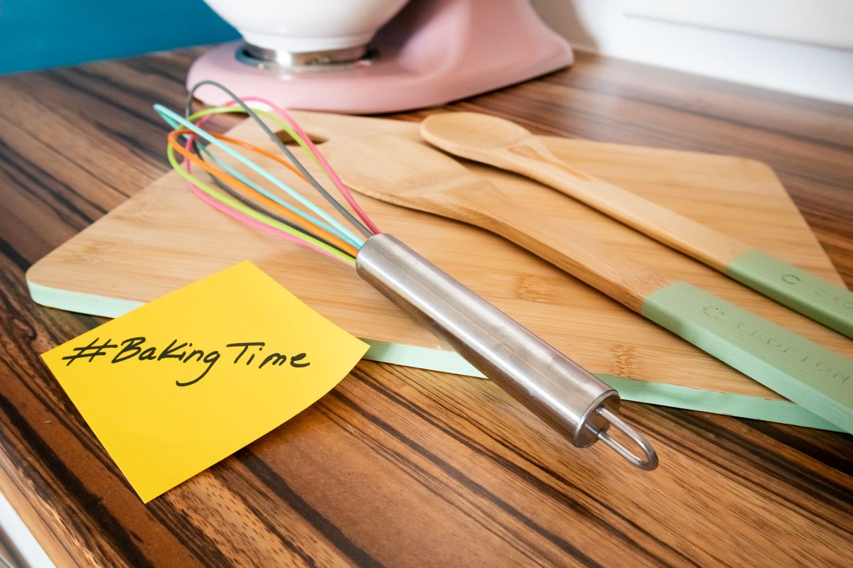 Colorful metal whisk with kitchen utensils on a wooden cutting board with #BakingTime note.