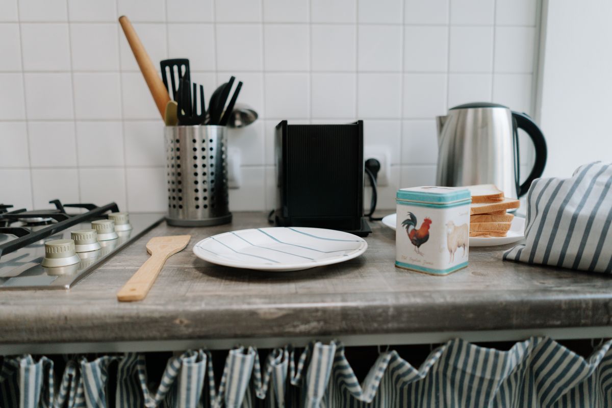 A clean kitchen counter featuring utensils, a kettle, and a tin can with vibrant design.