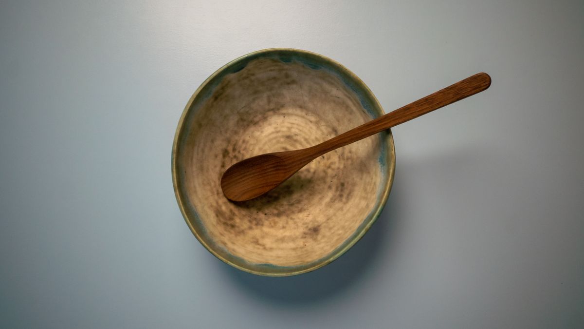 Top view of beige colored artisan bowl with wooden spoon placed on white table