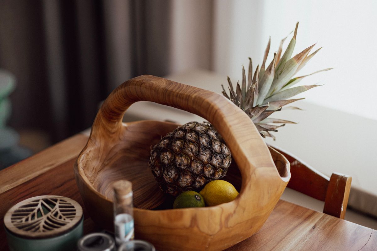 A rustic wooden bowl with pineapple and citrus fruits on a wooden table indoors.