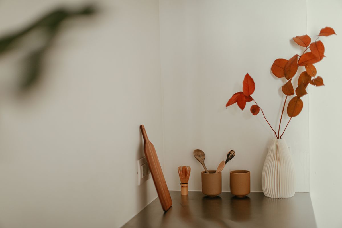 A serene minimalist kitchen corner featuring red leaves in a vase, wooden utensils, and cups.