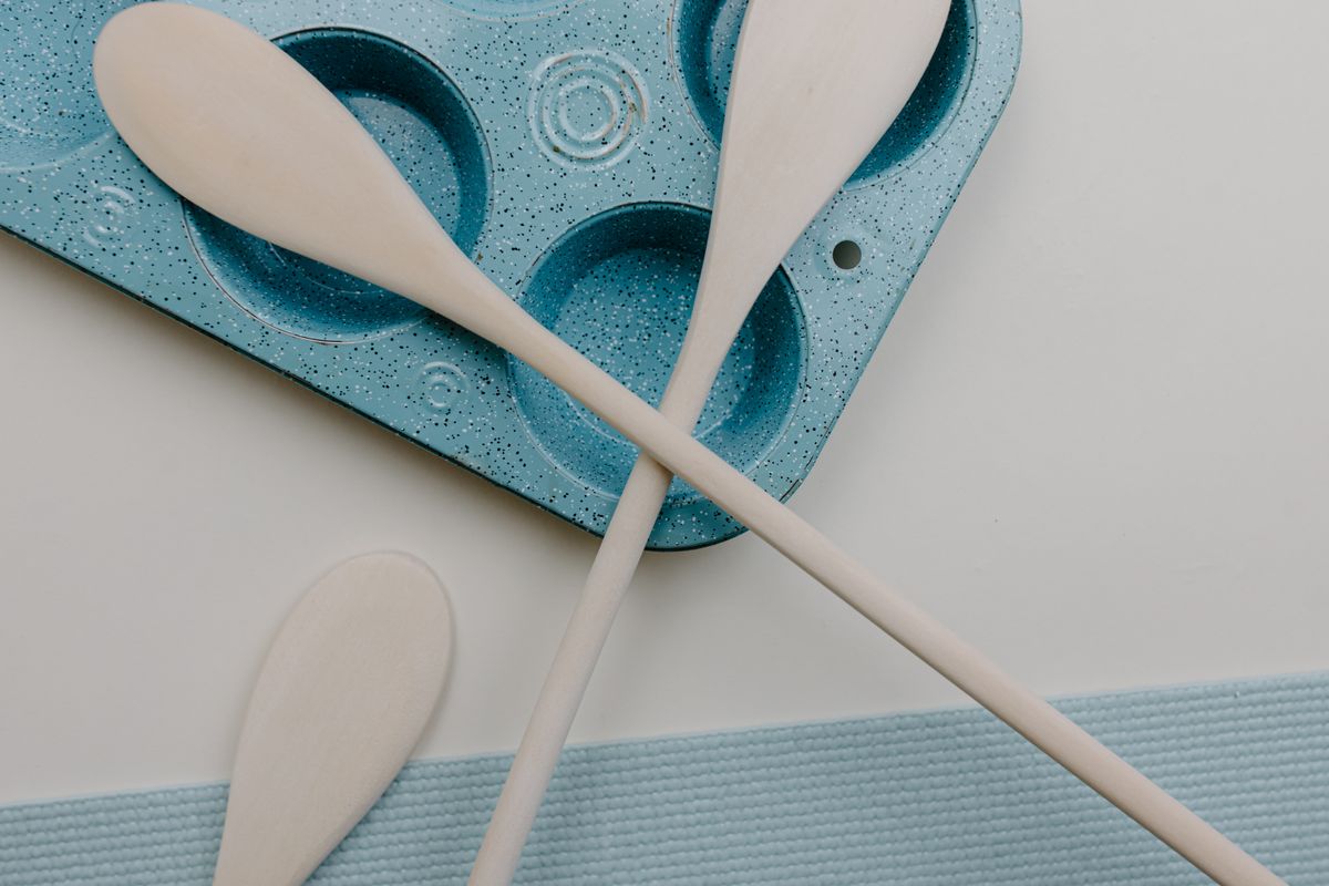 Minimalist kitchen scene with wooden spatulas and a blue baking tray on a white surface.