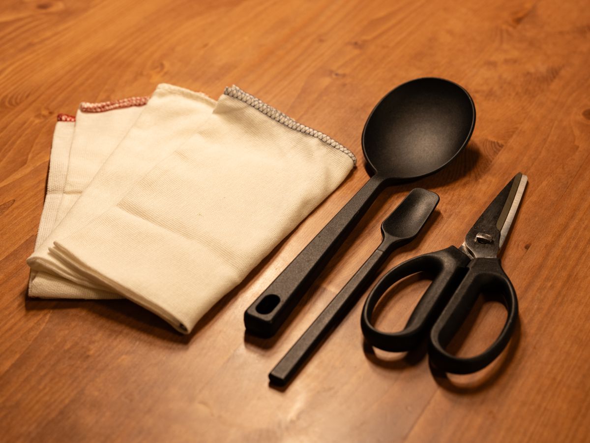 A collection of kitchen utensils including a spoon, spatula, and scissors on a wooden table.