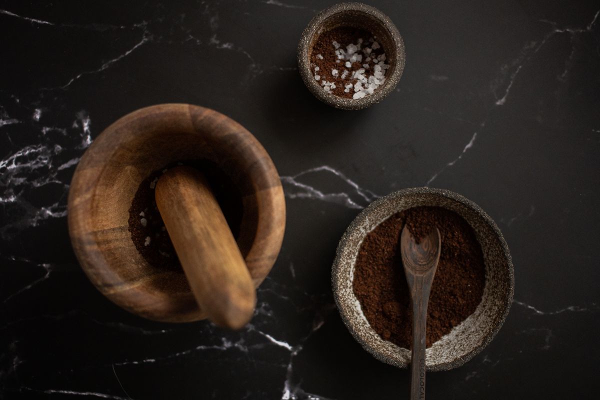 High angle of wooden mortar and pestle placed near ceramic bowl with aromatic coffee on black marble table