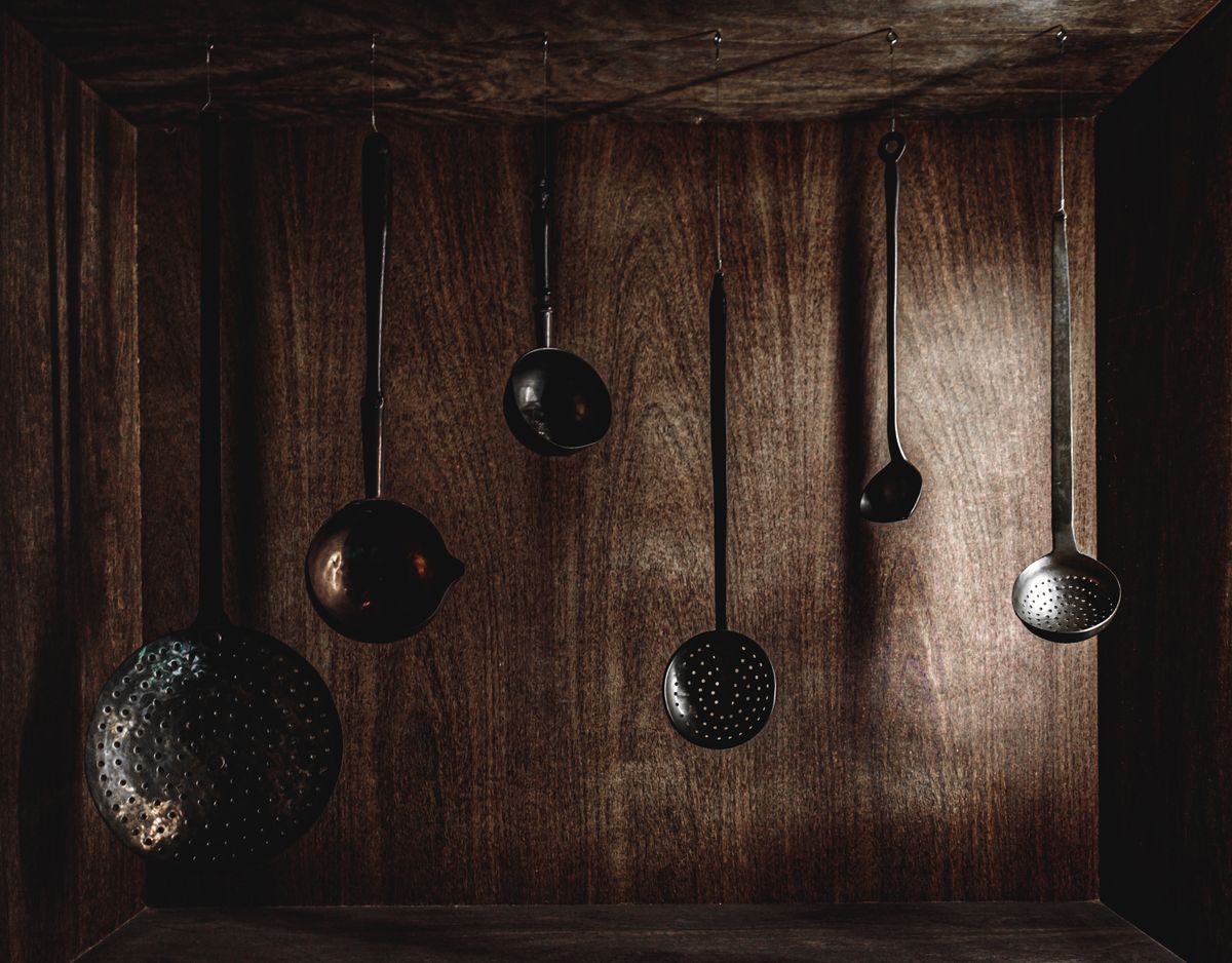 A vintage collection of metal kitchen utensils hanging on a rustic wood backdrop, perfect for culinary-inspired designs.