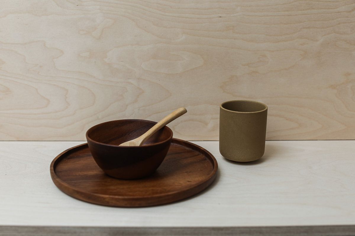 Simple still life of a wooden bowl and ceramic cup on a white table, showcasing minimalist design.