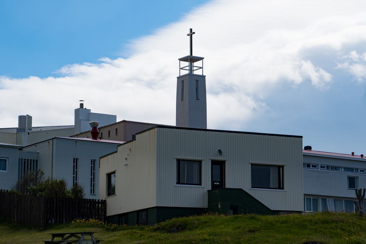 Contemporary white church building with cross tower against a bright blue sky.