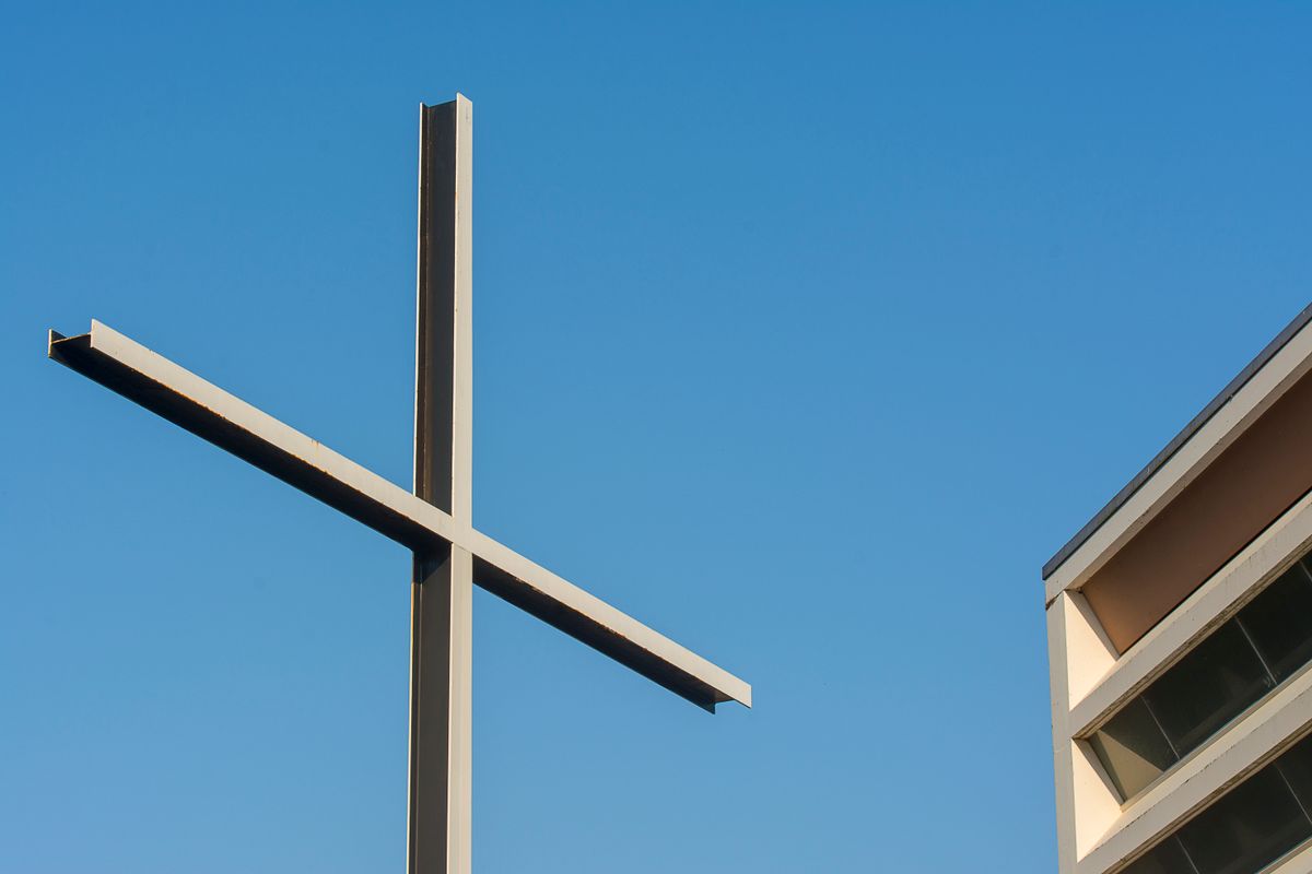 A minimalist cross beside a modern building against a clear blue sky, symbolizing simplicity and spirituality.