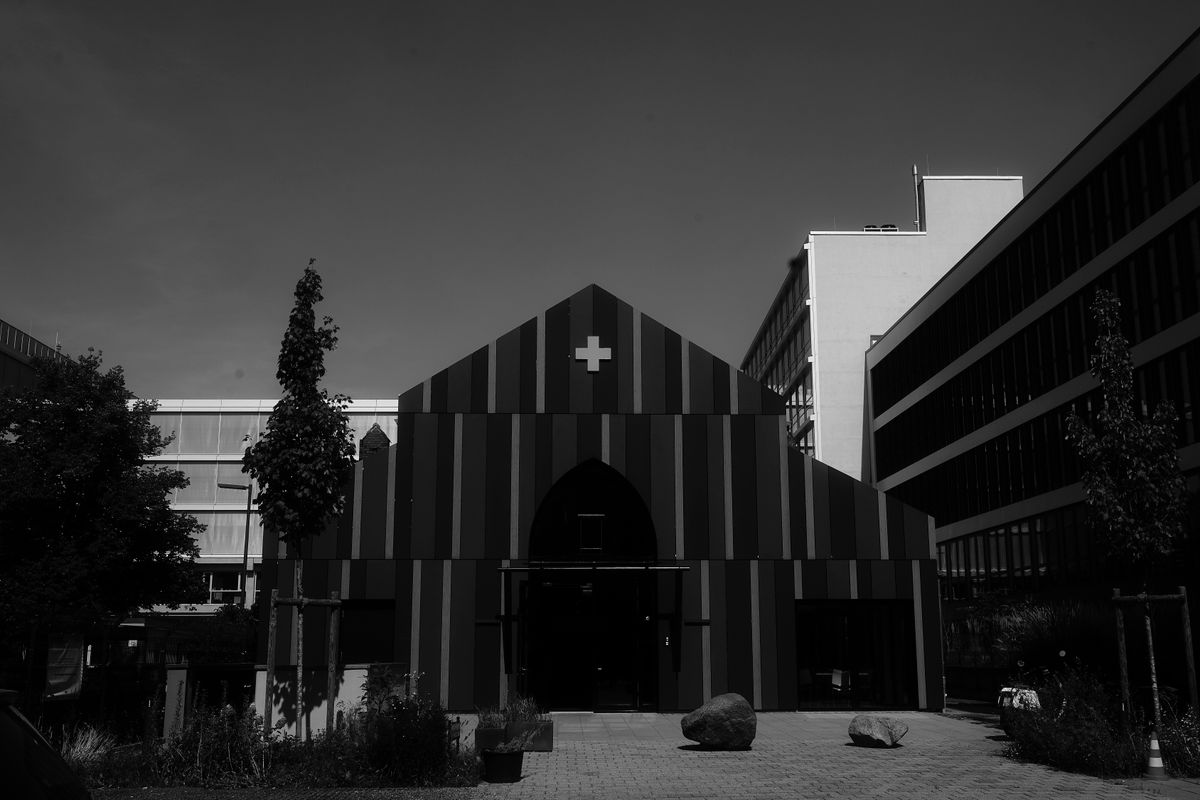 Black and white photo of a modern striped building with a cross, surrounded by urban architecture.
