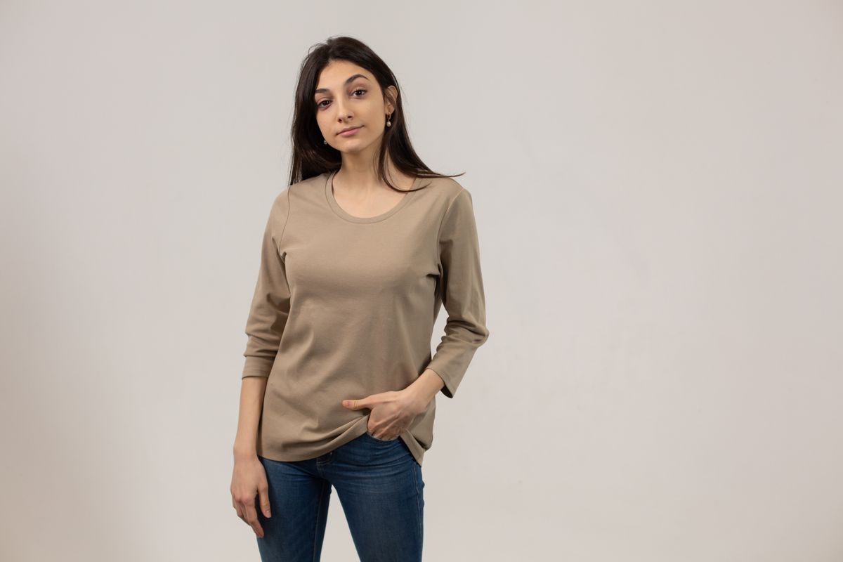 Content female wearing casual outfit and jeans looking away while standing on gray background with hand in pocket in studio