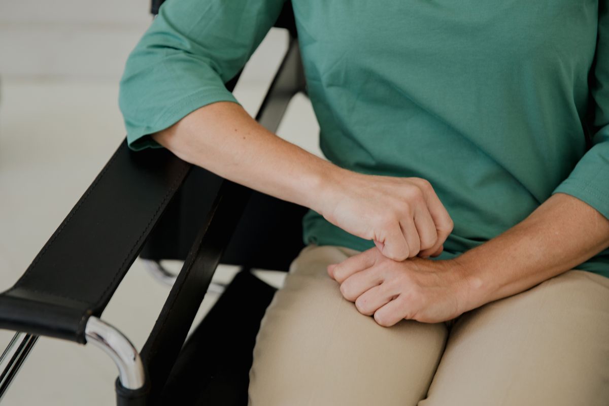 Detailed image of hands resting on a chair armrest, wearing a green shirt.