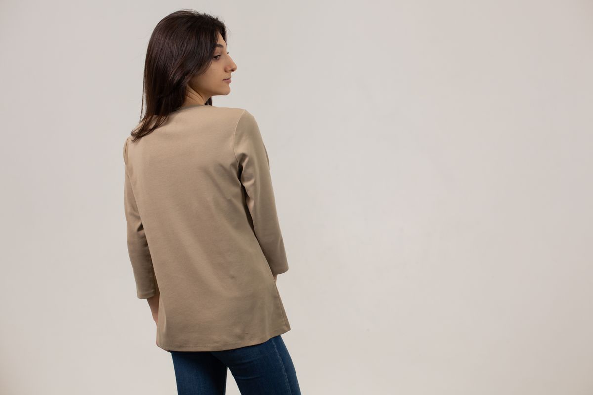 Back view of young female wearing long sleeve t shirt and jeans standing against white background and looking away