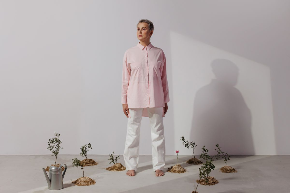 Studio portrait of woman in pink shirt and white pants with seedlings and watering can.