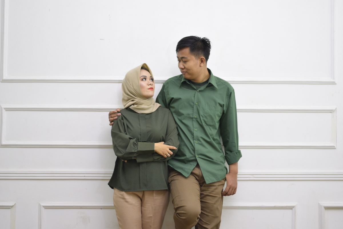 An affectionate couple poses against a white wall, showcasing a modern fashion style.