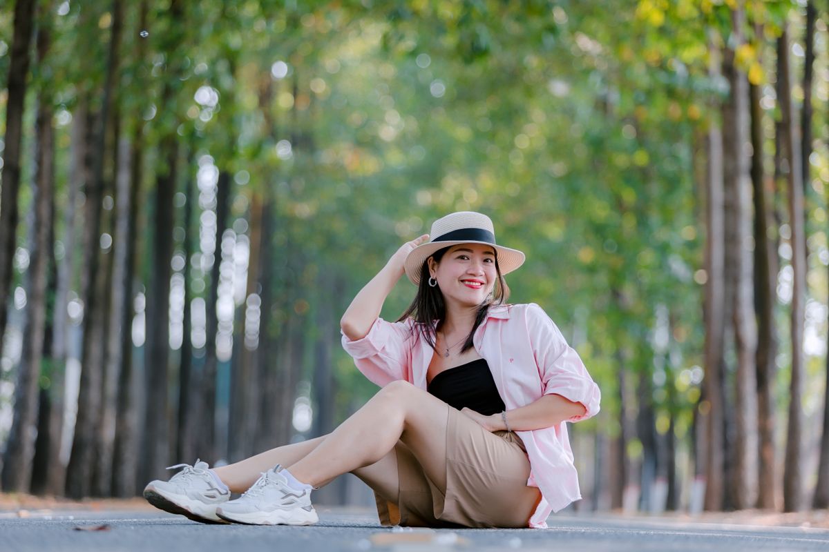 A cheerful woman enjoys a sunny day in the park, wearing a stylish hat and casual outfit.