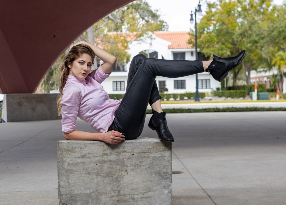 Young woman in a purple shirt and black pants posing stylishly outdoors on a concrete structure.