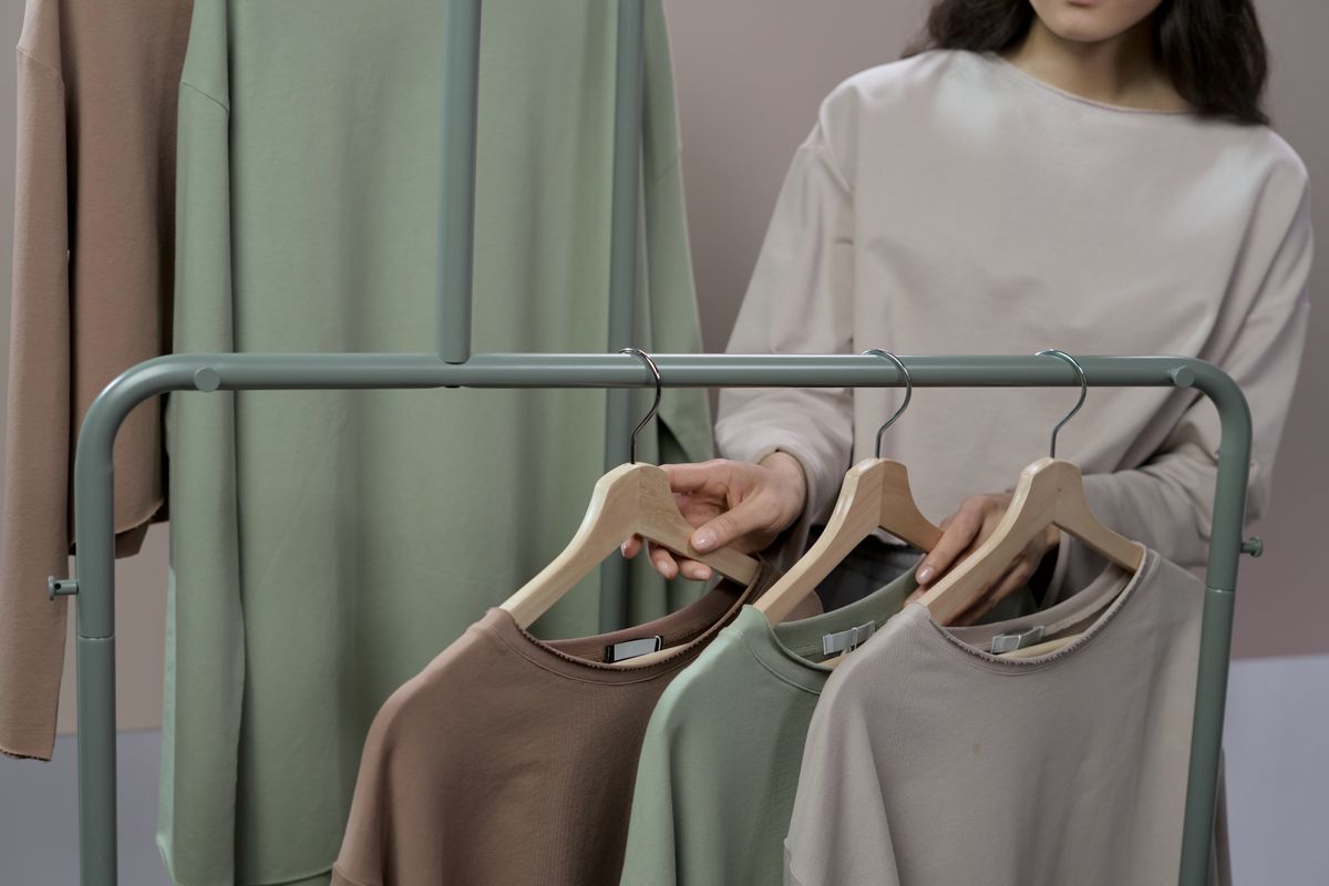 Woman choosing neutral colored sweaters from a clothing rack in a modern store.