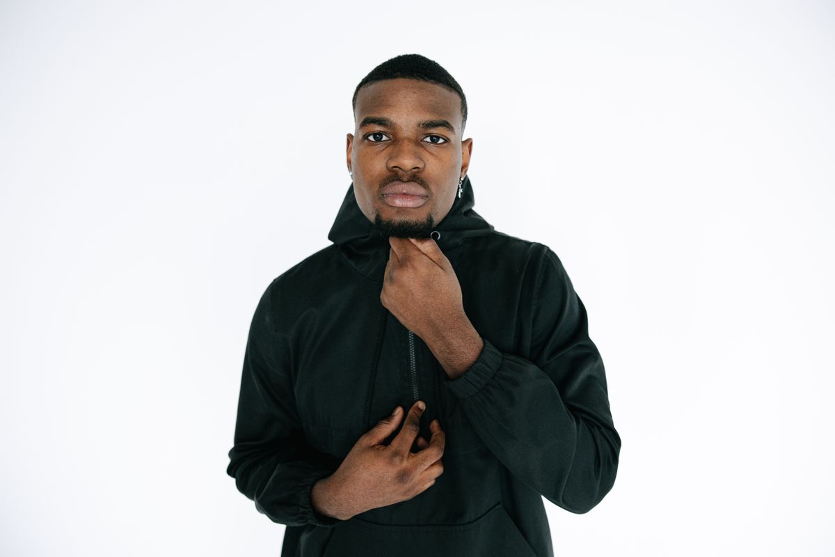 Studio portrait of a man in a black hooded jacket posing against a white background.