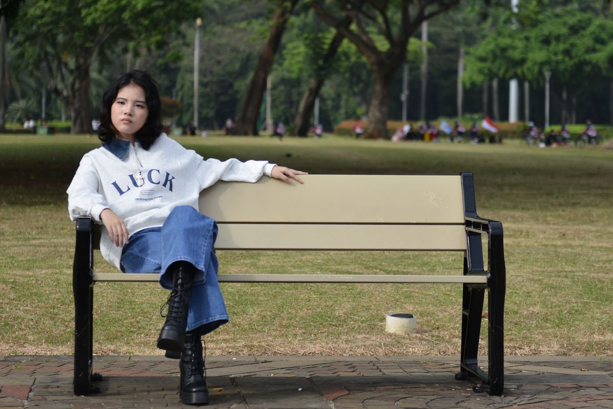 Young woman in stylish outfit sitting on a bench in a lush green park.
