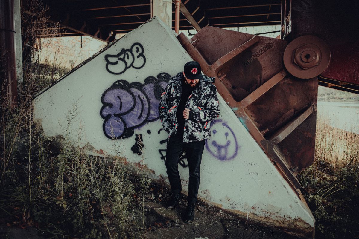 Model posing under bridge with graffiti, wearing casual fashion for a modern look.