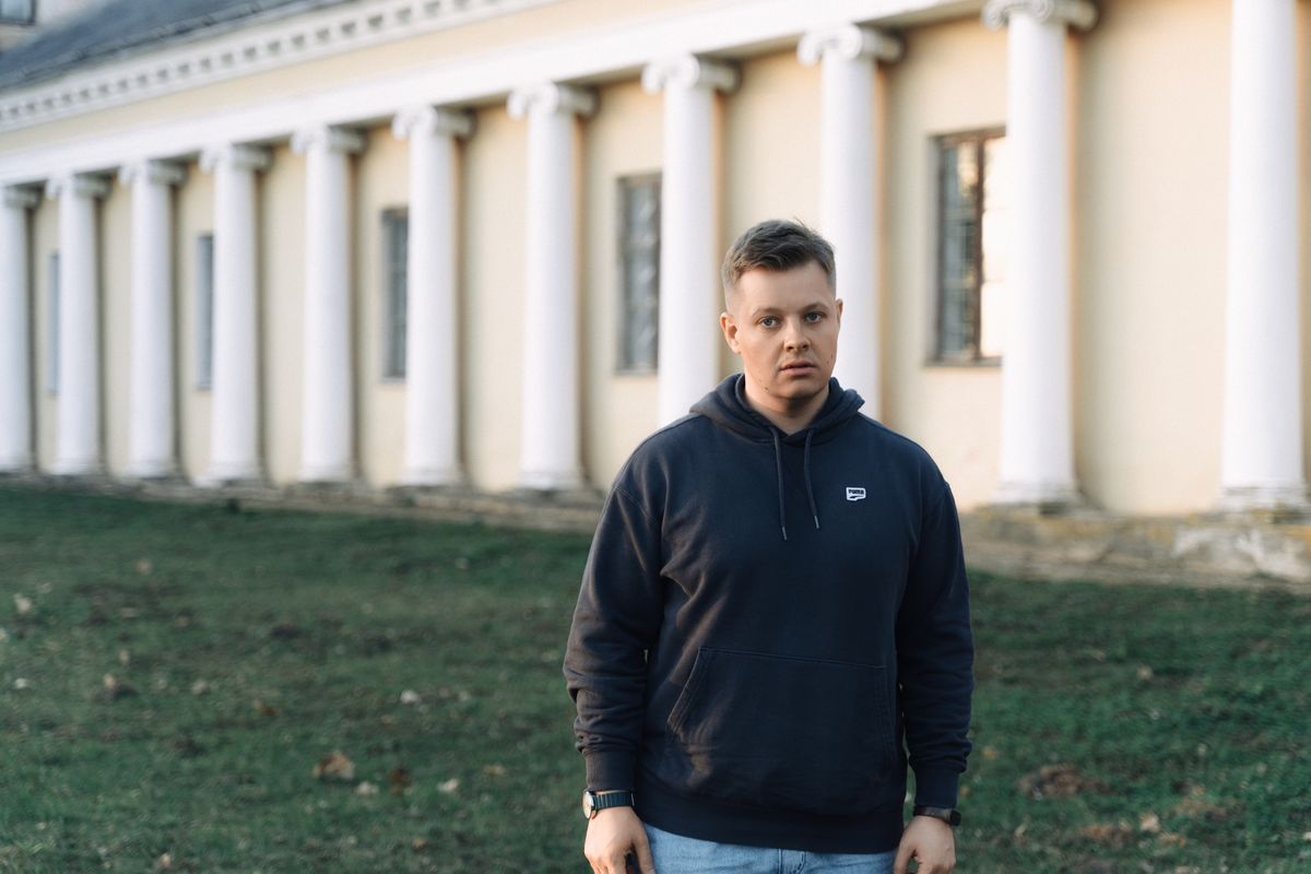 Man in hoodie standing outdoors by neoclassical building columns.