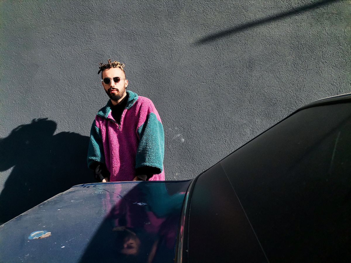 Fashionable man with sunglasses leaning on a car, dressed in a stylish wool coat.