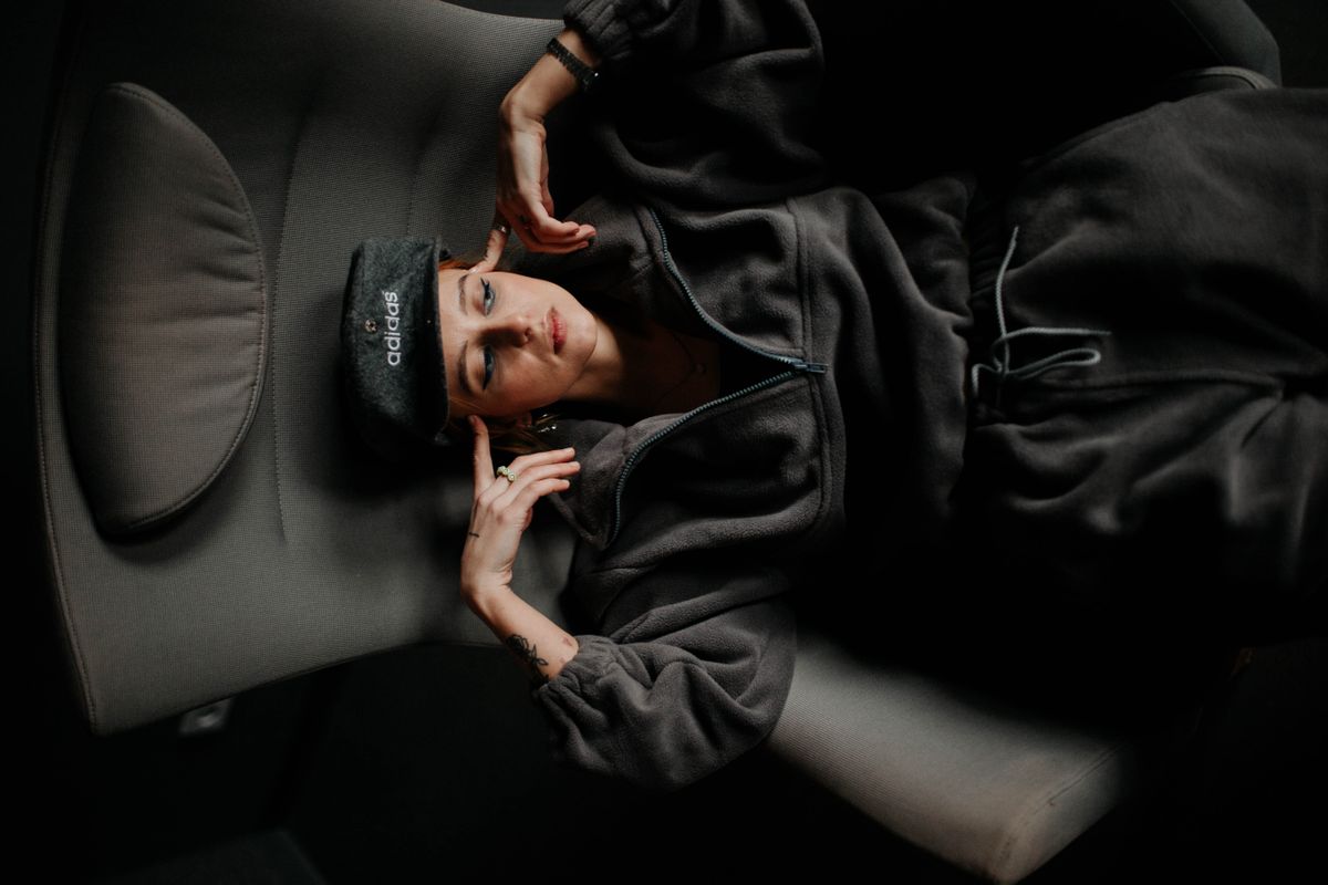 A young woman wearing a hoodie and cap lounges comfortably in an armchair, exemplifying relaxation and style.