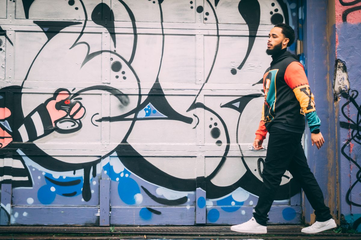 A man in vibrant attire walks past a colorful graffiti mural, showcasing urban street style.