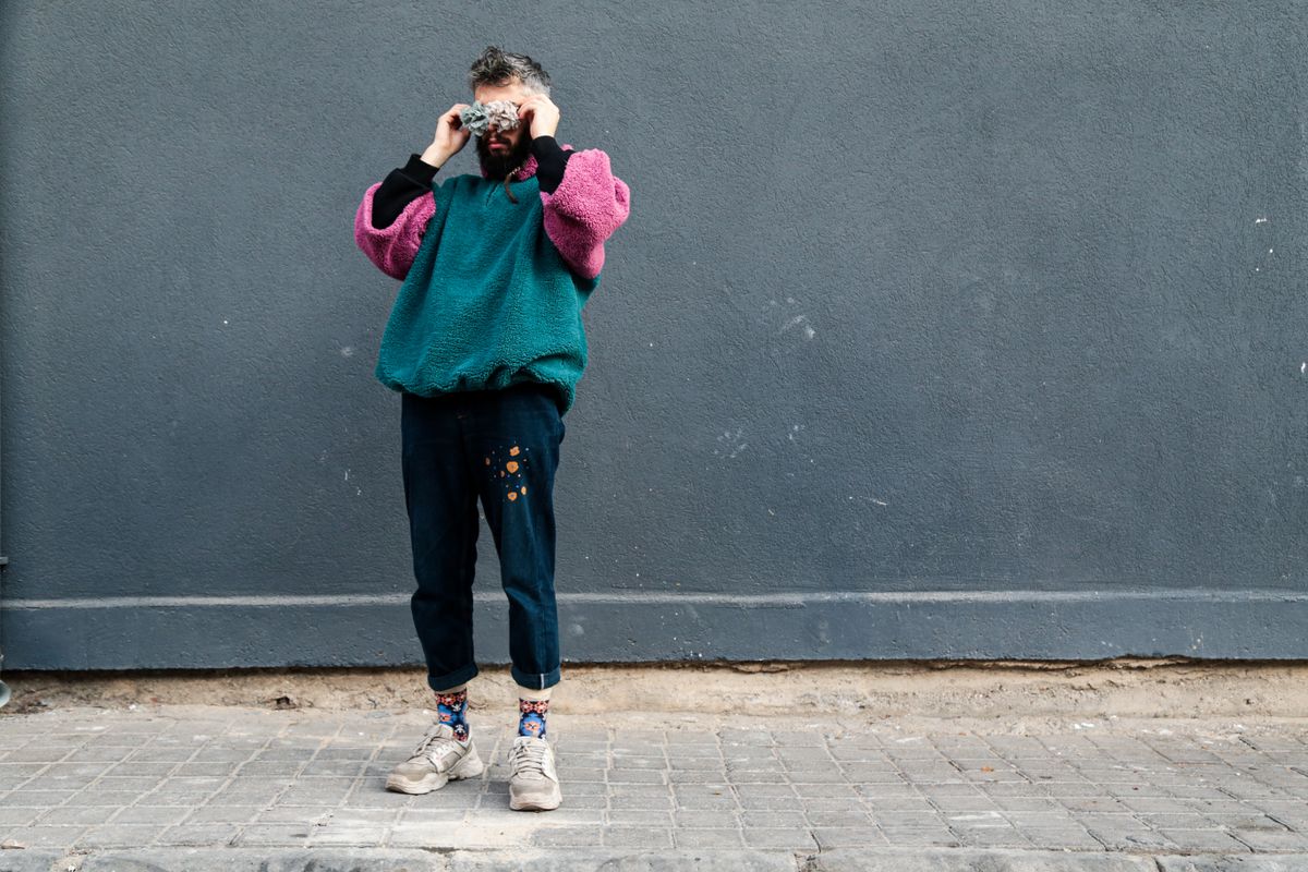 Fashion model wearing colorful sweater and denim poses against gray urban wall.