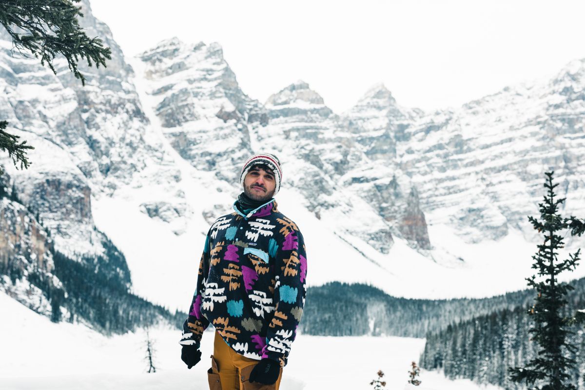 Man wearing a colorful jacket stands amidst the snow-capped mountains of Banff, Canada, embracing winter adventure.