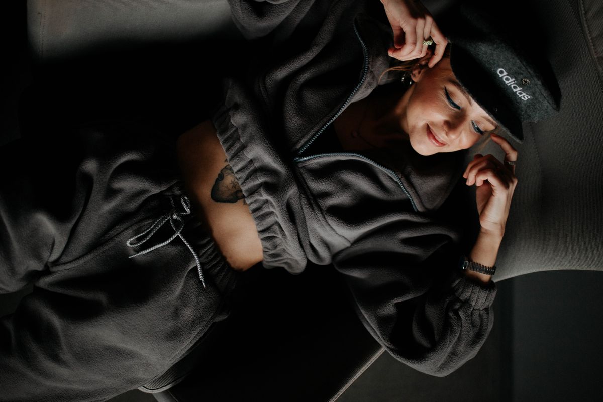 A stylish woman in an Adidas hat and loungewear poses comfortably indoors, showcasing modern fashion.