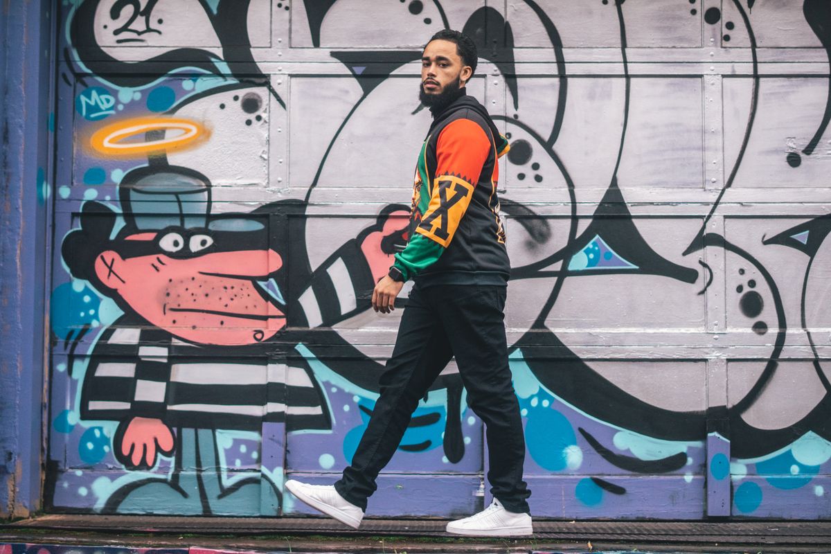Stylish man walking past vibrant graffiti wall, showcasing urban fashion and art.