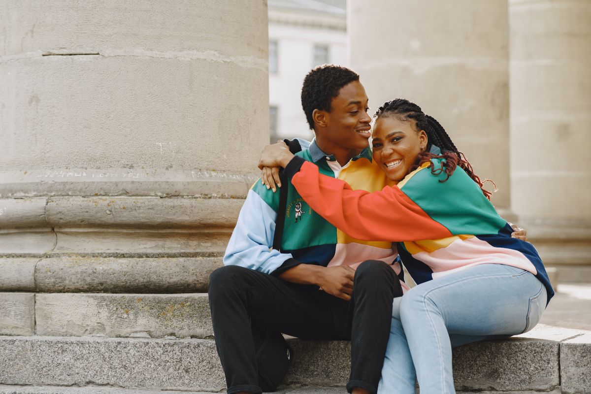 Smiling couple embracing while sitting on ancient stone stairs, wearing colorful clothes.