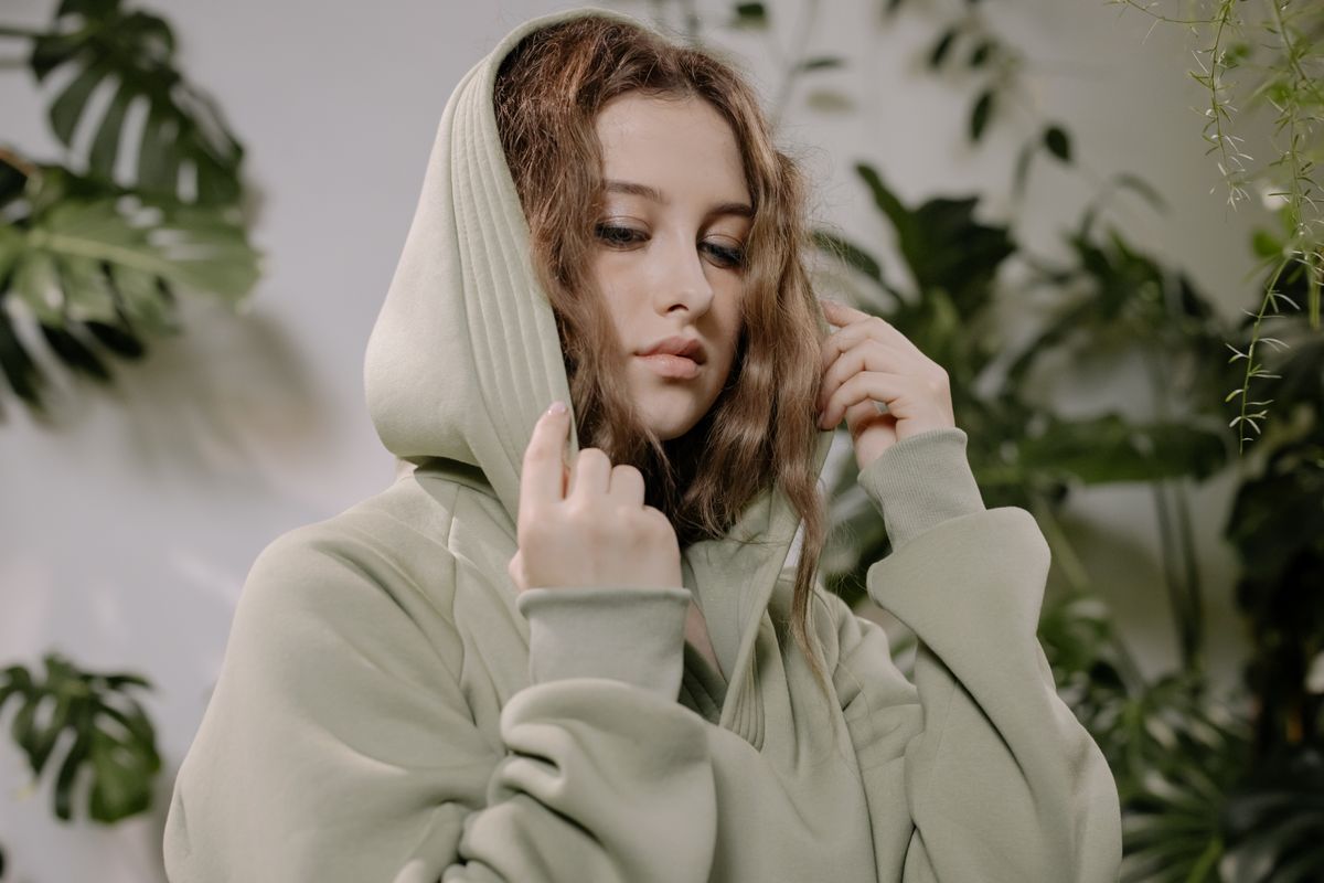 Portrait of a woman wearing a hoodie with curly hair, surrounded by greenery indoors.