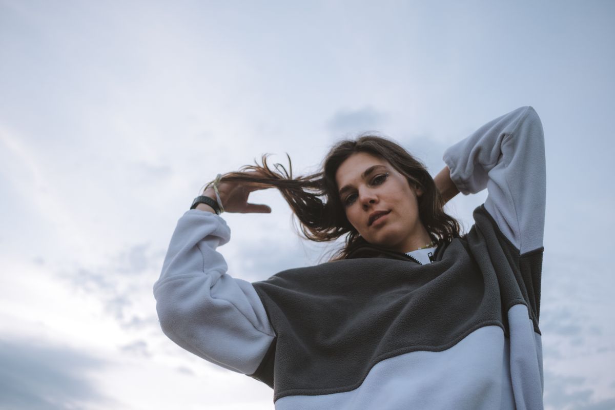 Stylish young woman poses in casual streetwear against a cloudy sky, embodying modern street fashion.
