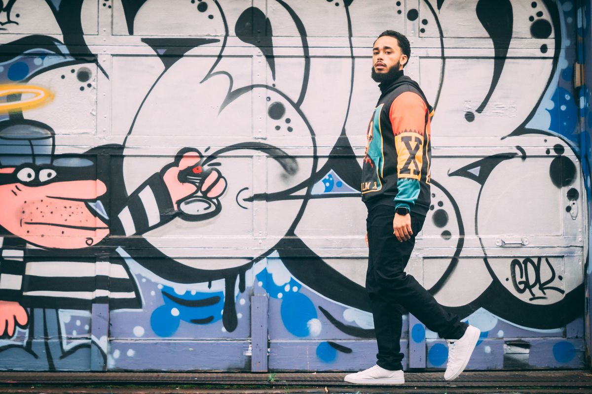 A man walking past colorful street art mural on urban wall, exuding modern style.
