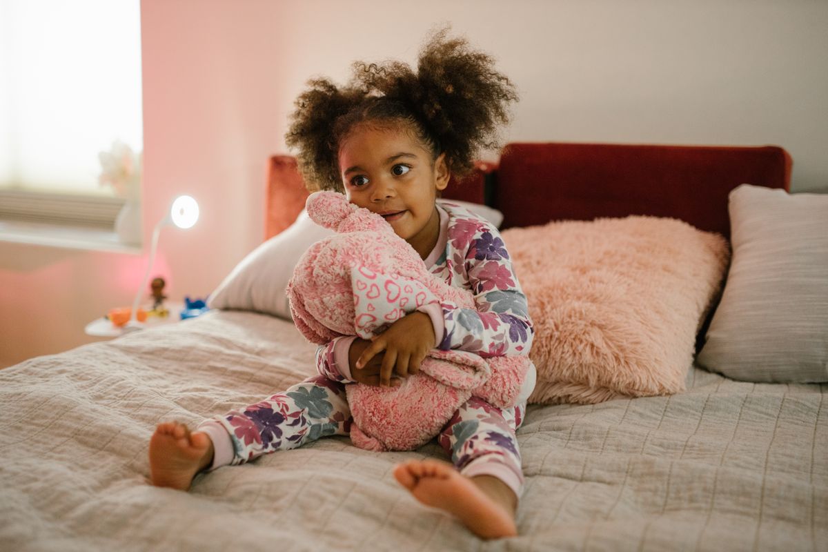 Cute child sitting on a bed hugging a plush toy, creating a warm and cozy atmosphere.