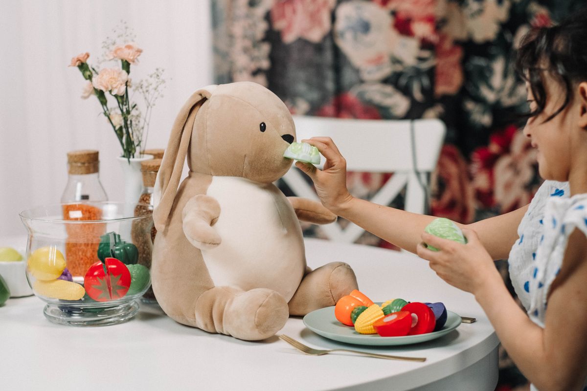 A child enjoying playful interaction with a plush bunny toy at a dining table setup.