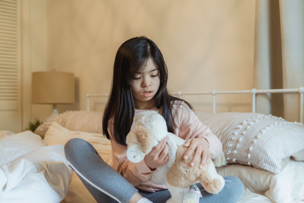 A child plays with a plush toy in a cozy bedroom setting, surrounded by pillows.
