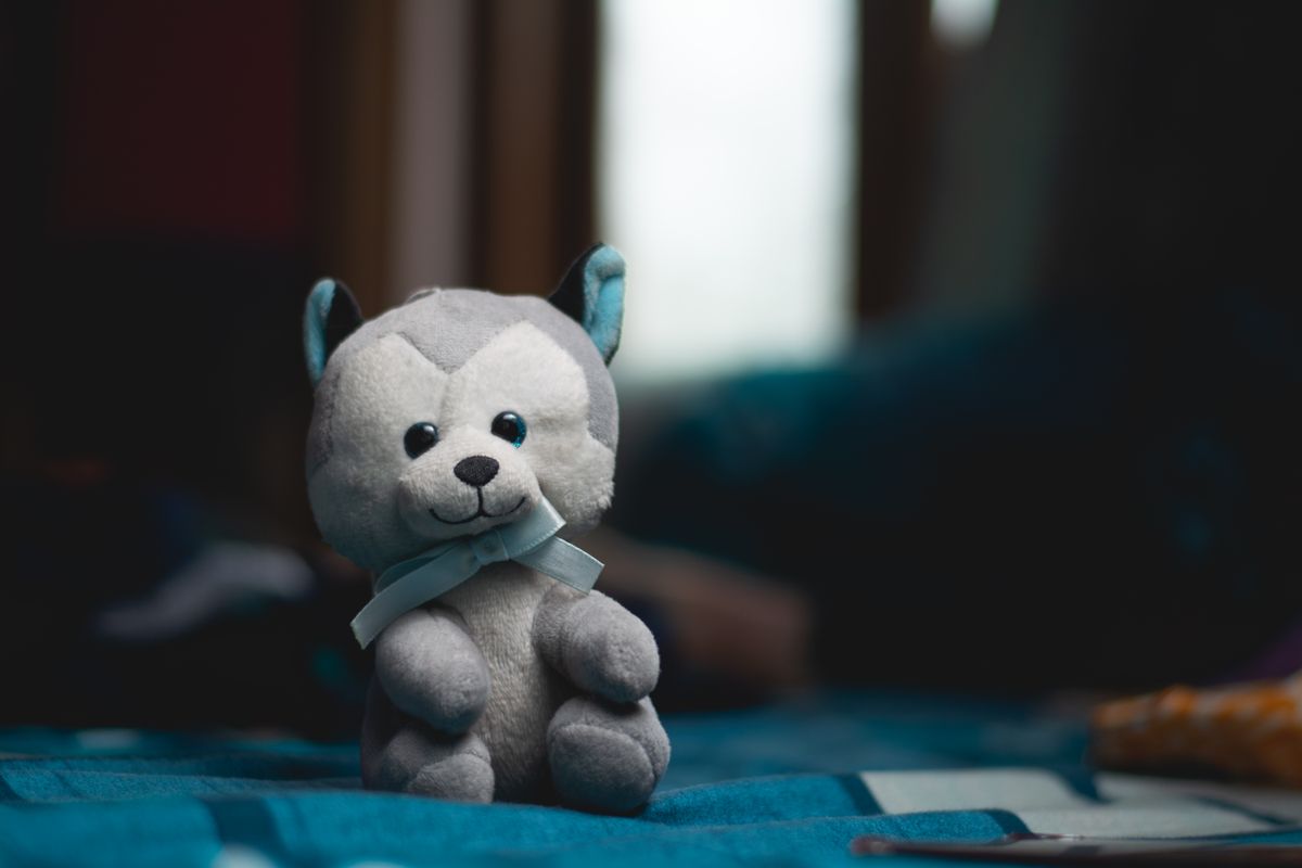 Cute plush stuffed toy husky dog with a bow tie sitting on a blue bedspread indoors.