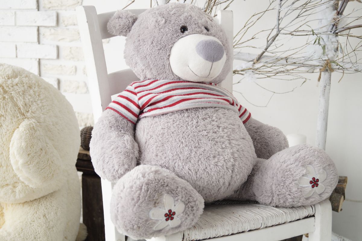 Adorable gray teddy bear wearing a striped shirt, sitting on a white chair, perfect for a child's room decor.