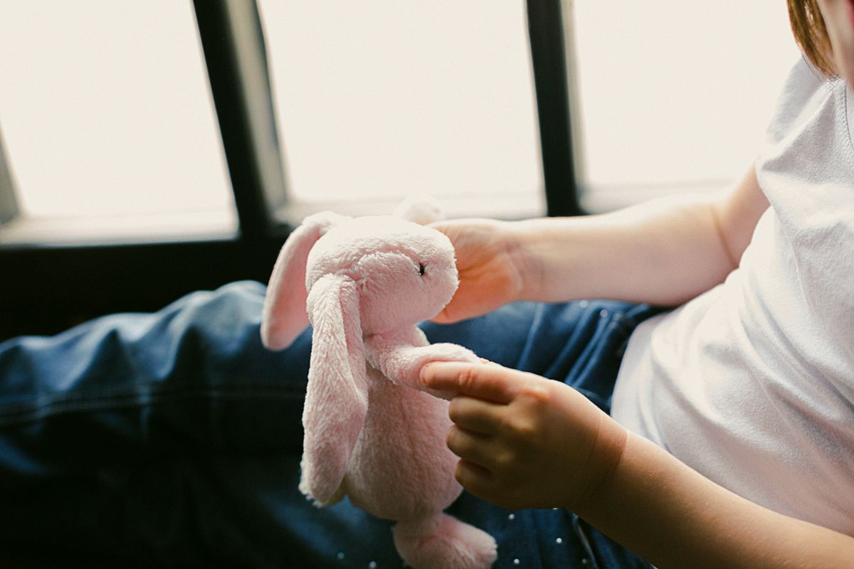 A cozy moment of a child holding a pink plush bunny toy by the window, conveying comfort and warmth.
