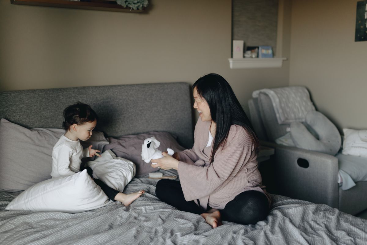 A mother and child share a loving moment while playing with a stuffed animal in a cozy bedroom setting.