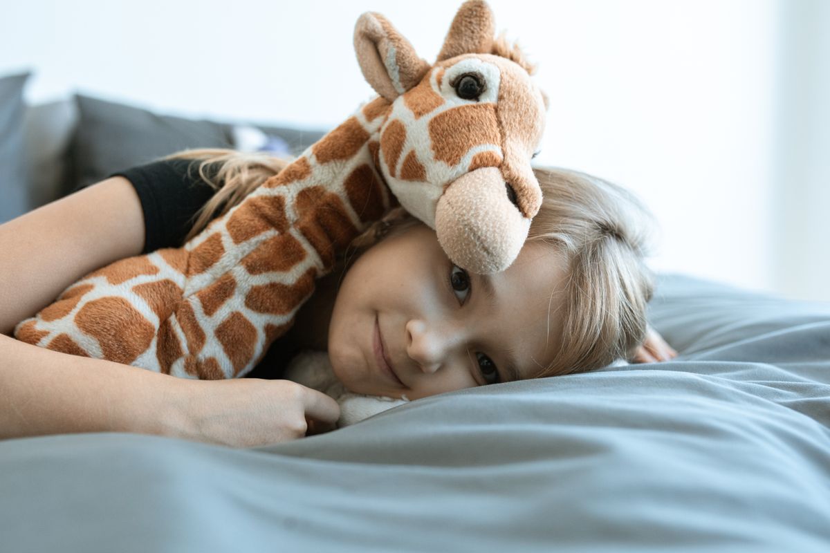 A child resting in bed hugging a giraffe plush toy, enjoying a cozy indoor atmosphere.