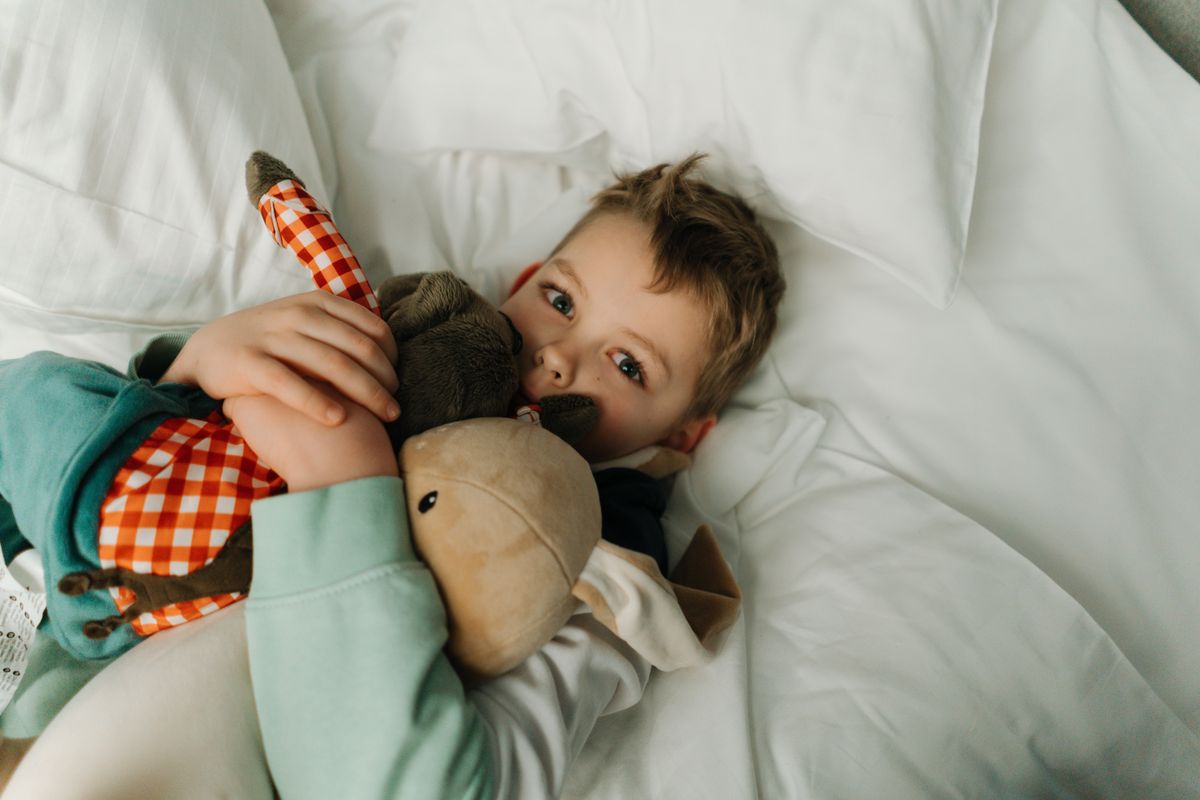A young child cuddles stuffed toys while resting on a bed, a scene of warmth and relaxation.