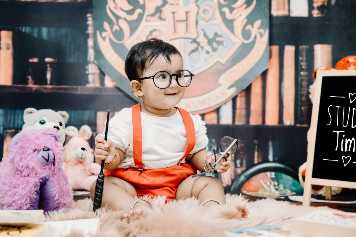 Charming baby dressed like a wizard with plush toys and a study theme setup.