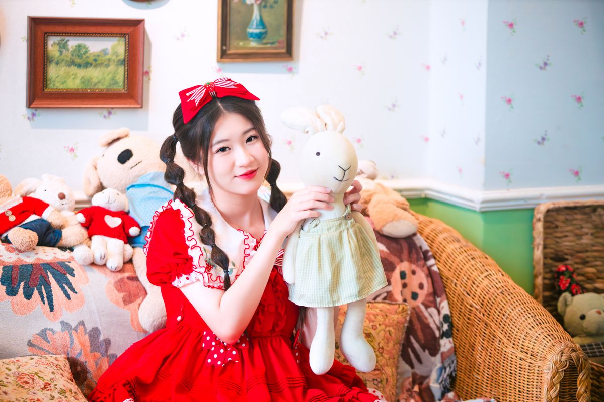 A young girl in a red dress holding a plush rabbit toy in a cozy room.