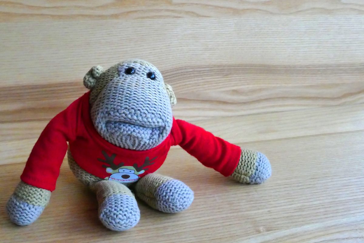 Cute knitted monkey toy in red attire sitting on a wooden surface, ideal for children's decor.