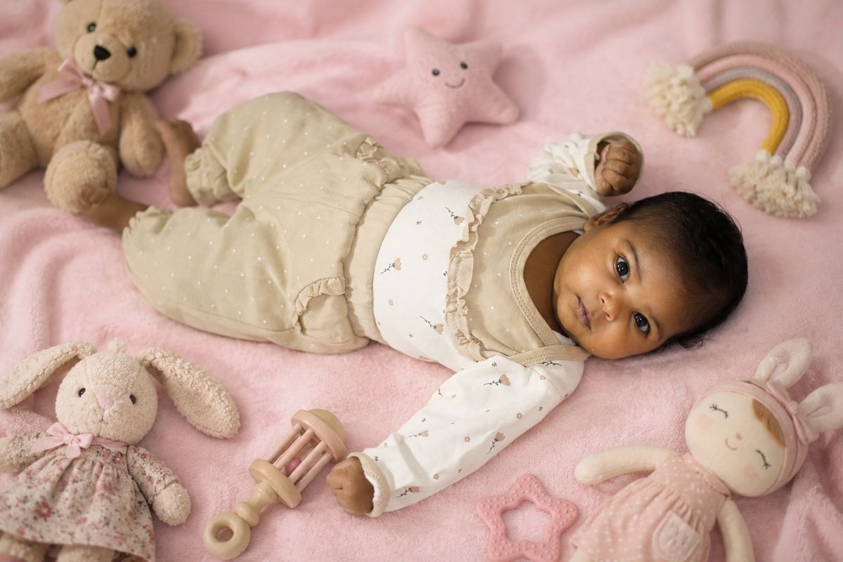 Charming baby surrounded by plush toys on a pink blanket. Perfect for nursery or children's decor themes.