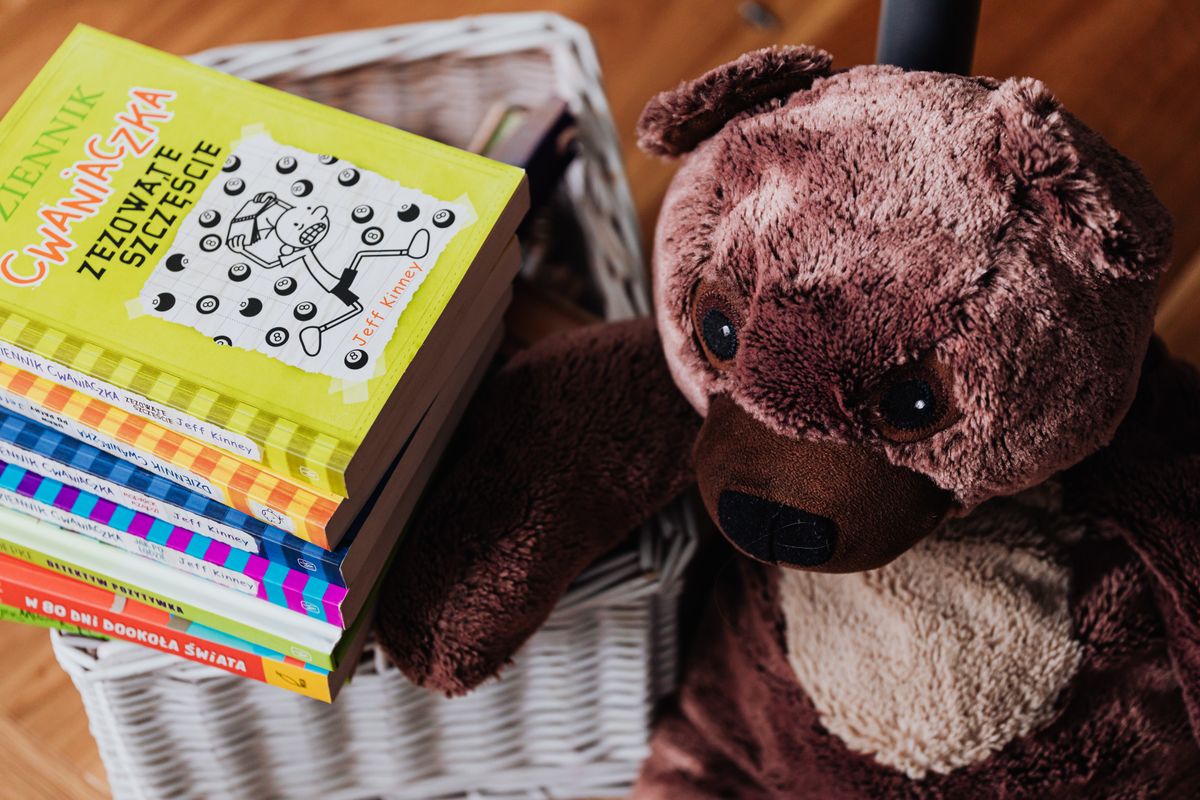 A stack of colorful children's books next to a plush teddy bear in a cozy kids' room.